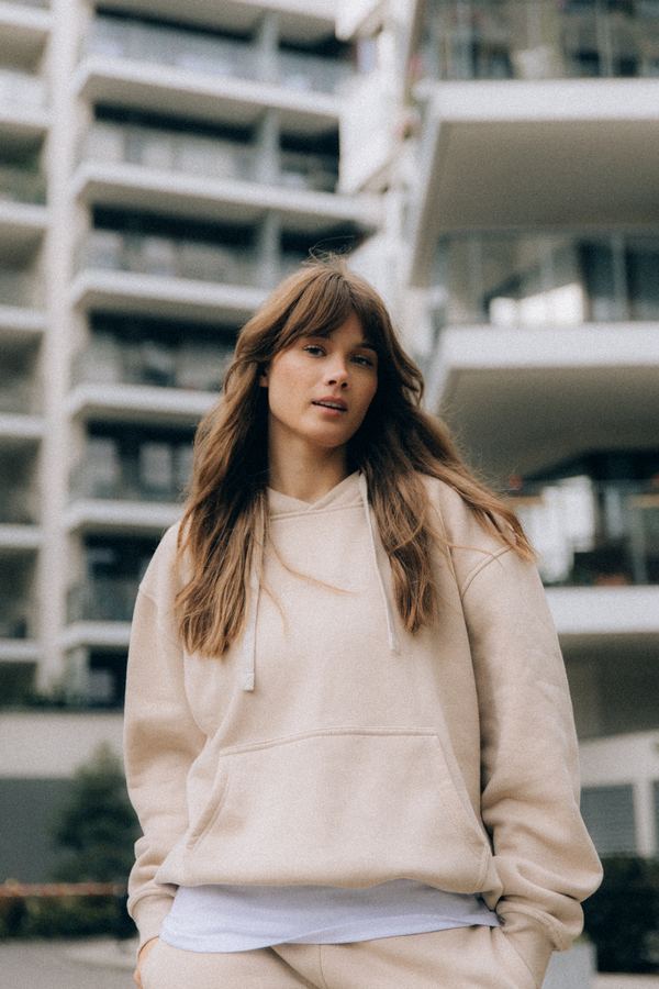 Modelka w beżowej bluzie oversize z kapturem na tle nowoczesnych budynków