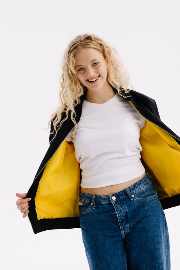 Modelka rozchyla czarną bluzę rozpinaną z żółtą podszewką